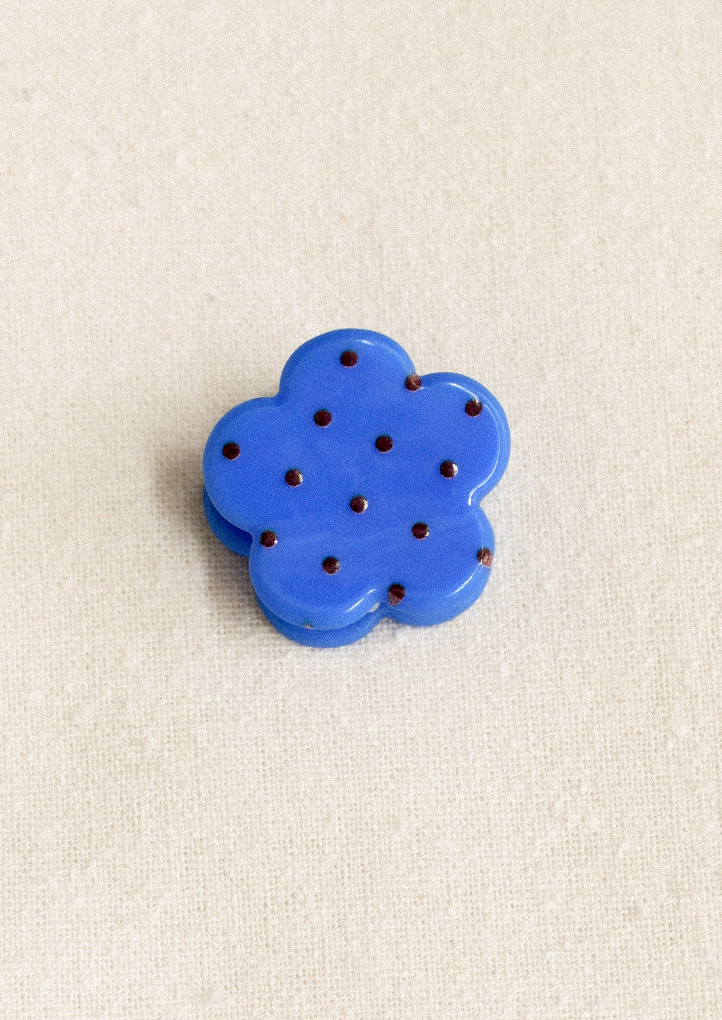 A small flower shaped hair clip in blue with burgundy polka dots.