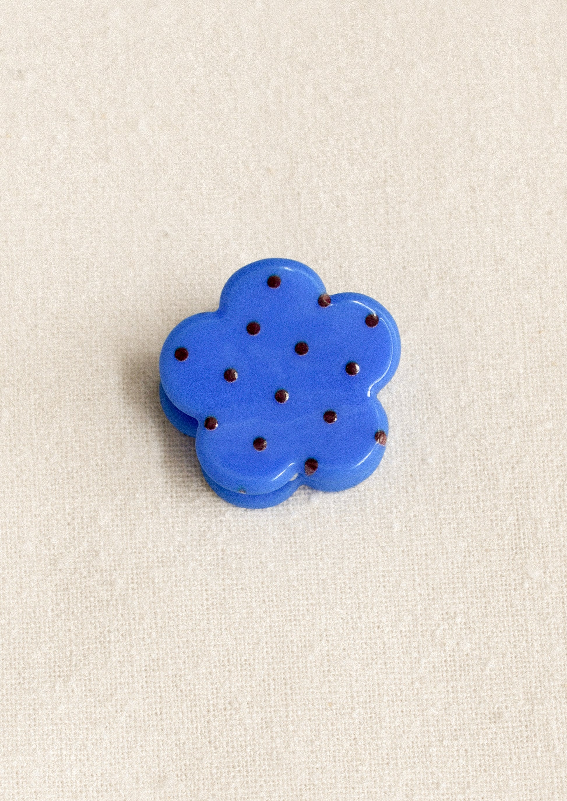 A small flower shaped hair clip in blue with burgundy polka dots.