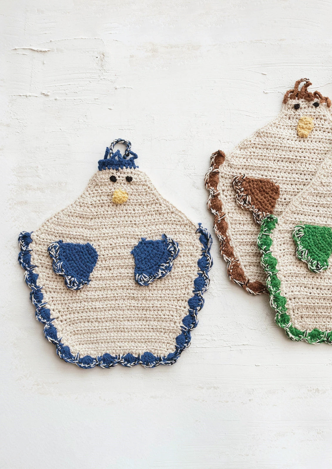 A crocheted potholder in the shape of a chicken, with blue detailing.