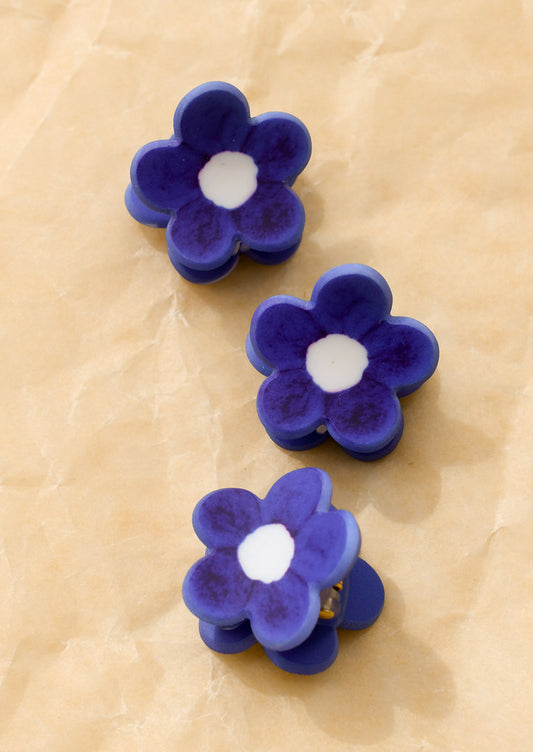 Three miniature hair claws in the shape of a flower, in matte cobalt blue with white centers.