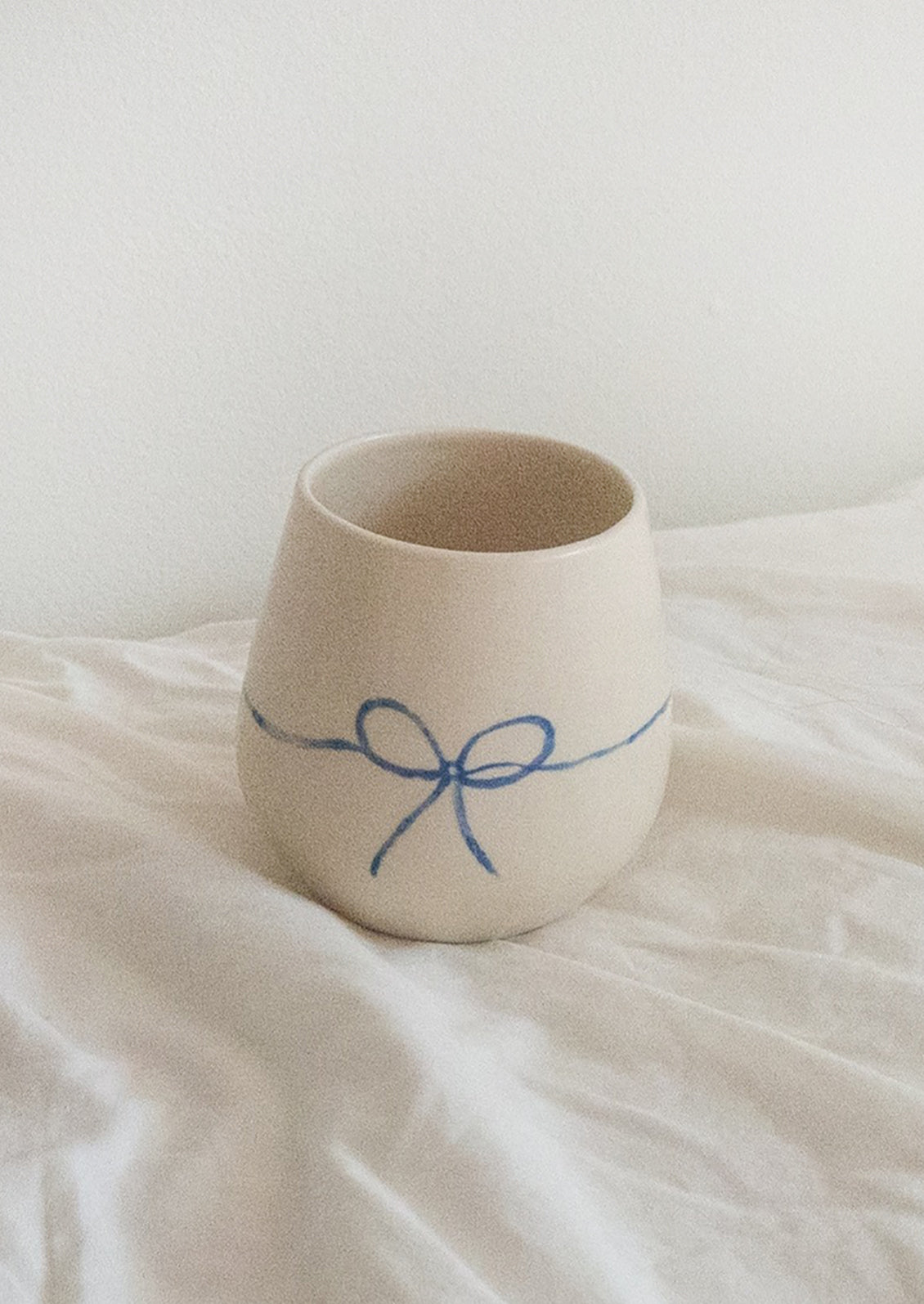 A white rounded ceramic cup with hand painted blue bow.