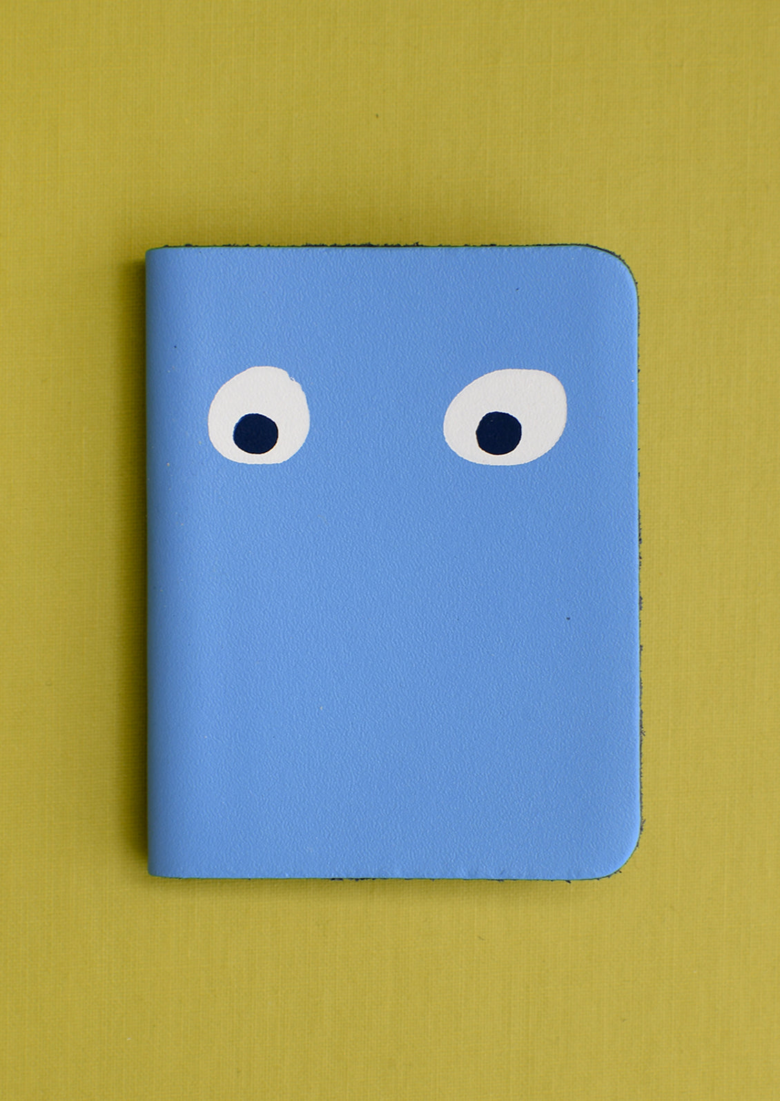 A blue leather notebook with pair of eyes painted on cover.