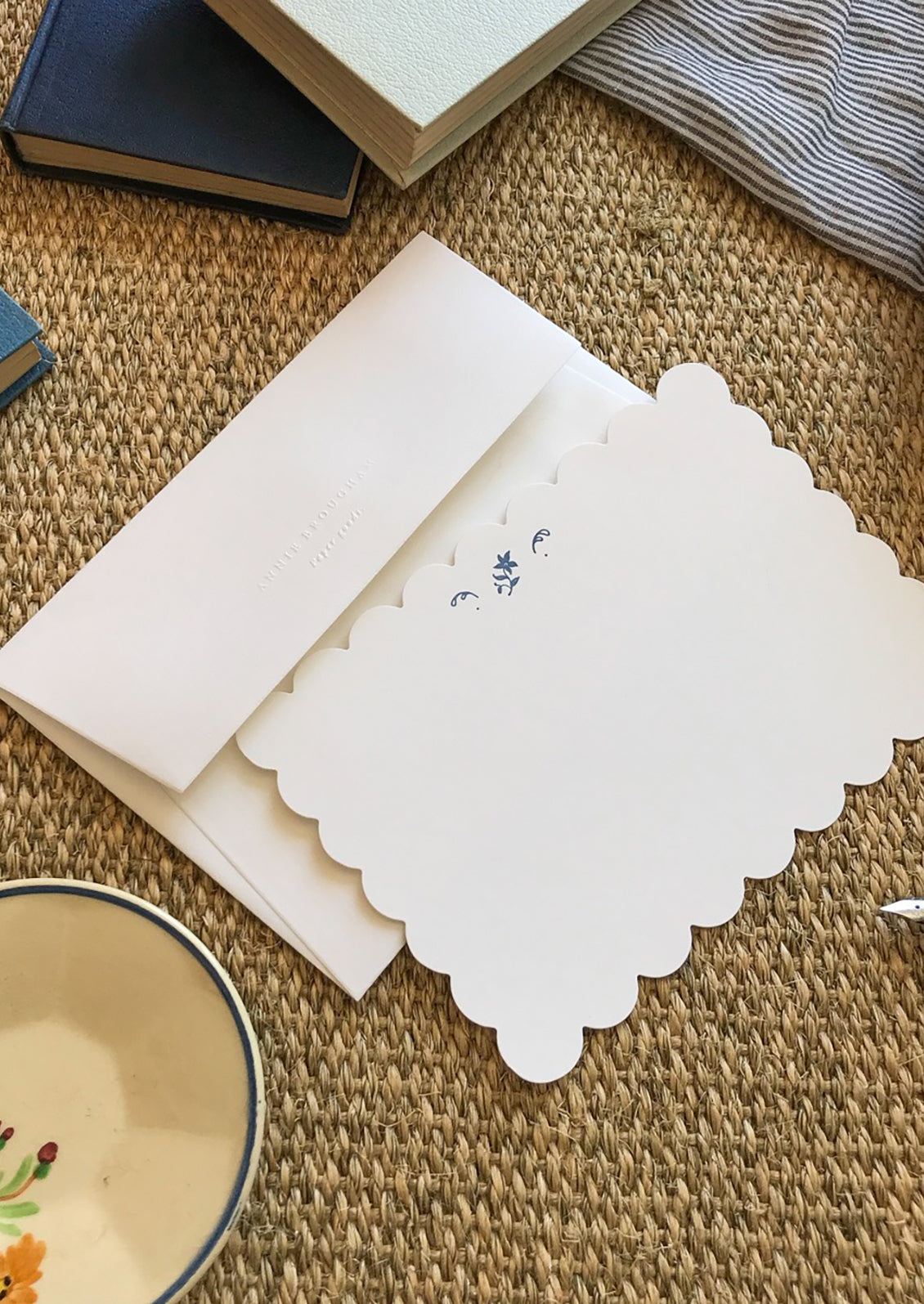 A scalloped white notecard with blue flower and white envelope.