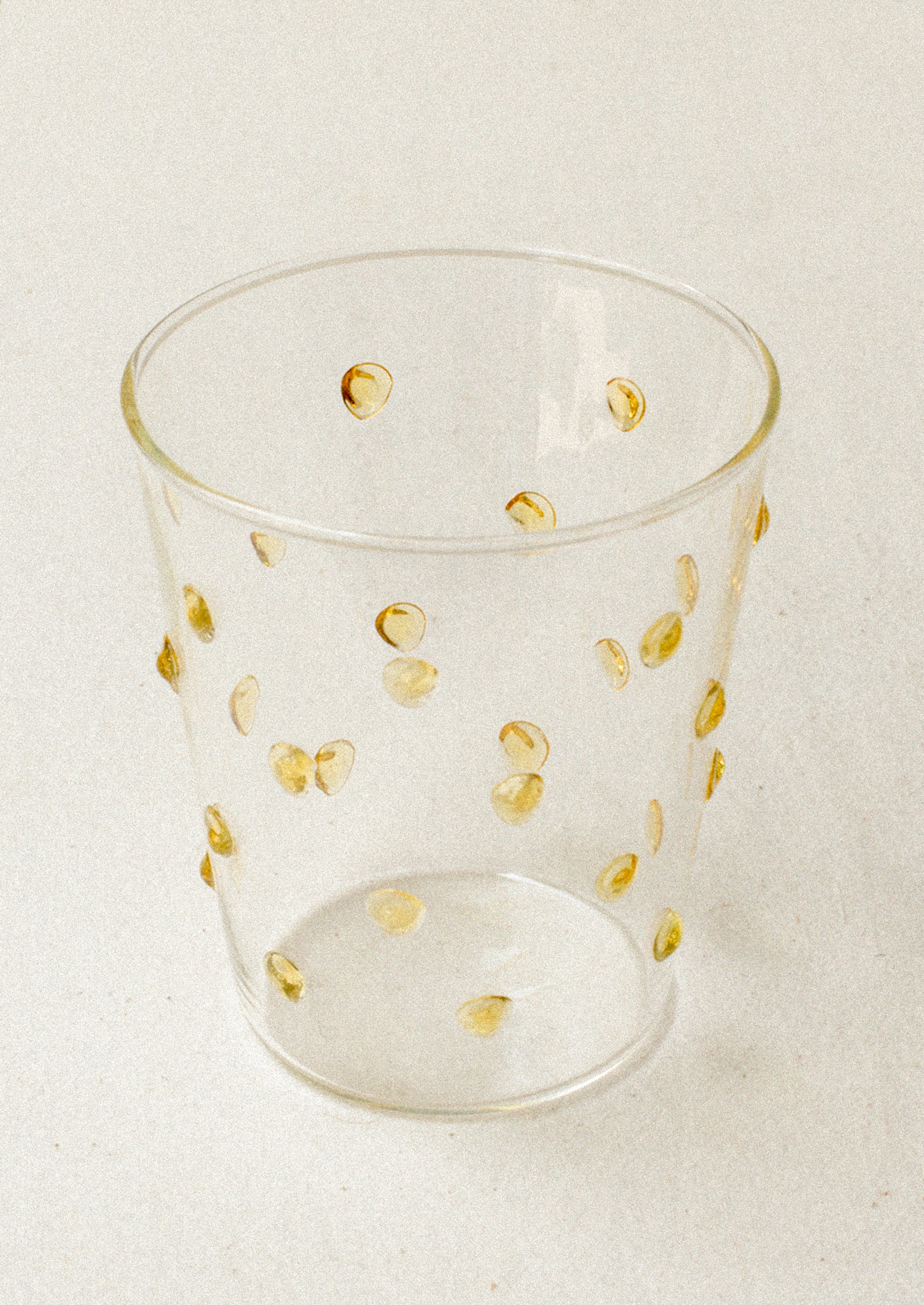 A clear glass tumblerswith textured raised dots on outside, in yellow.