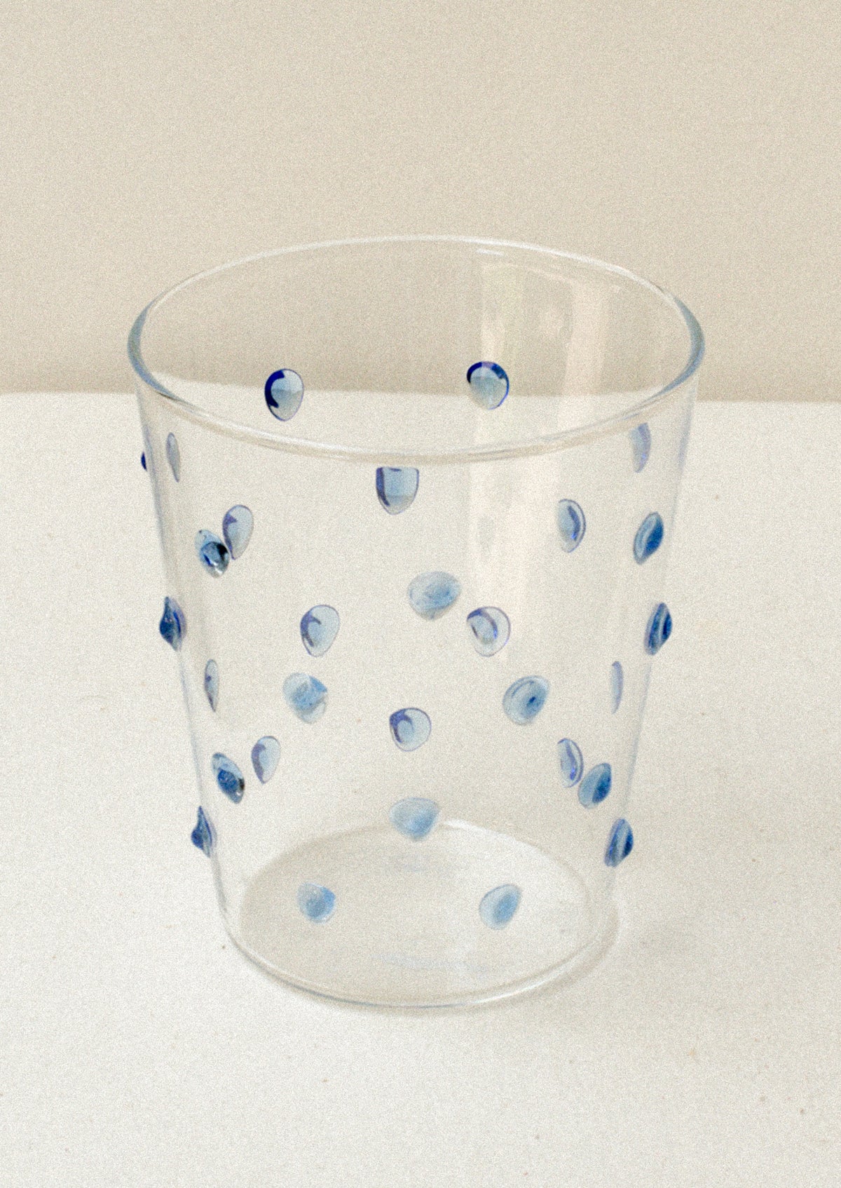 A clear glass tumblerswith textured raised dots on outside, in blue.