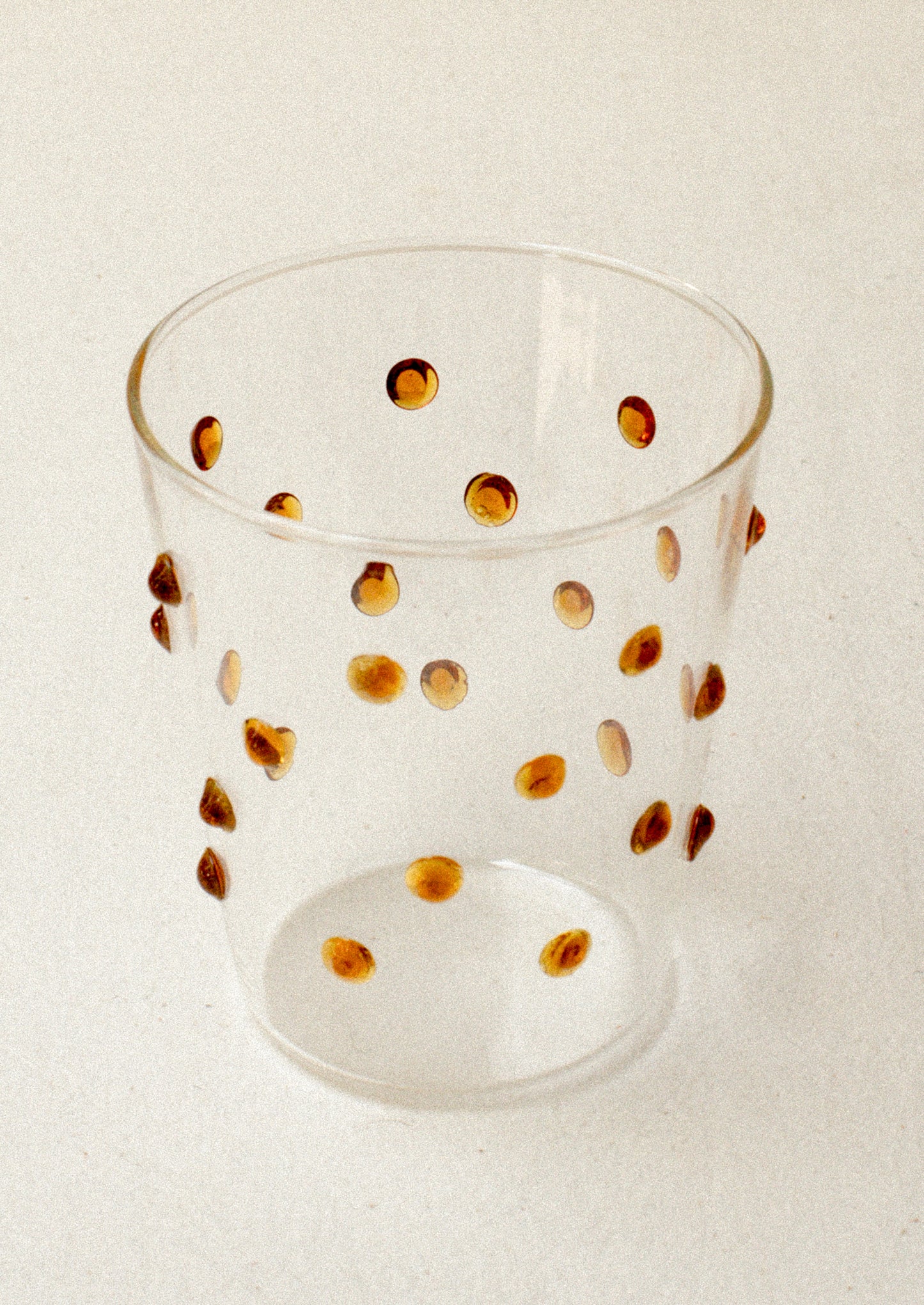 A clear glass tumblerswith textured raised dots on outside, in caramel.