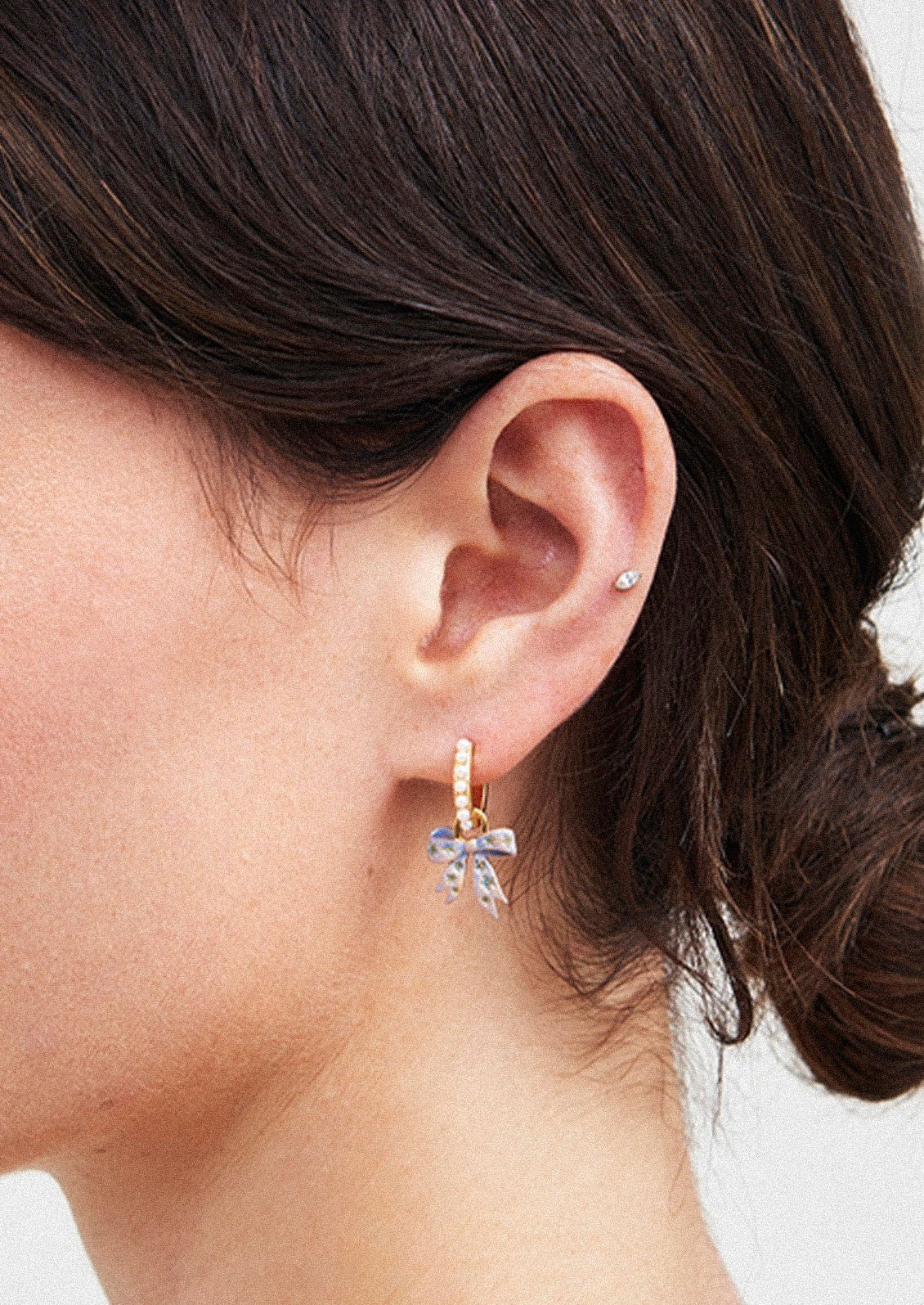 A pair of gold hoop earrings adorned with faux pearls and a bow charm.