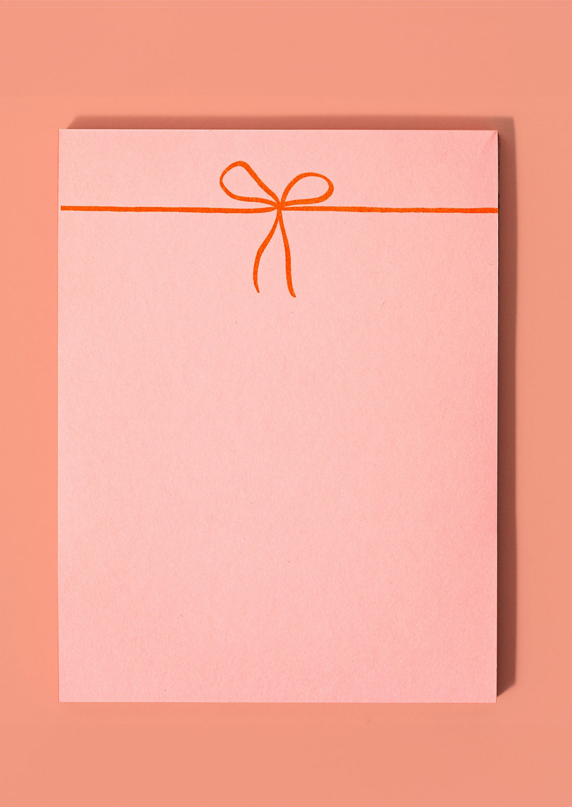 A pink notepad with neon orange printed bow.