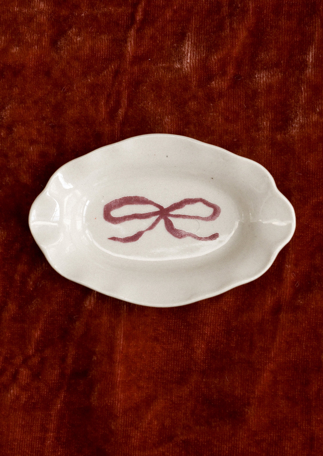 A small porcelain dish with ornate shape and hand painted bow illustration in red.