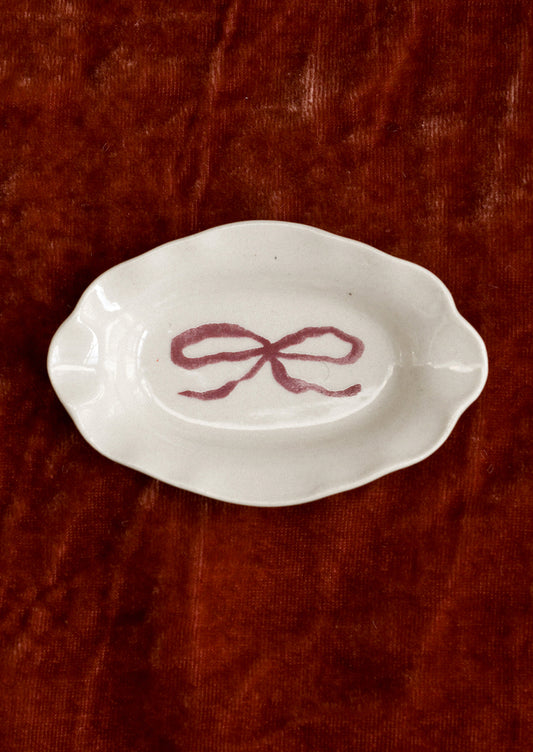 A small porcelain dish with ornate shape and hand painted bow illustration in red.