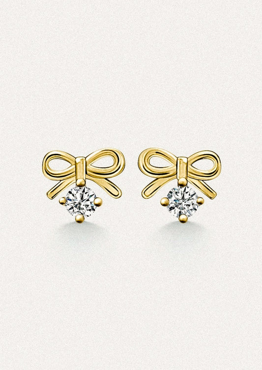 A pair of small gold stud earrings in the shape of a bow, with dangling cubic zirconia.