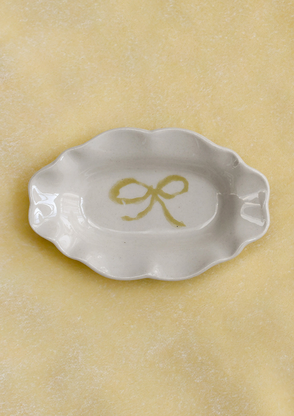 A small porcelain dish with ornate shape and hand painted bow illustration in yellow.