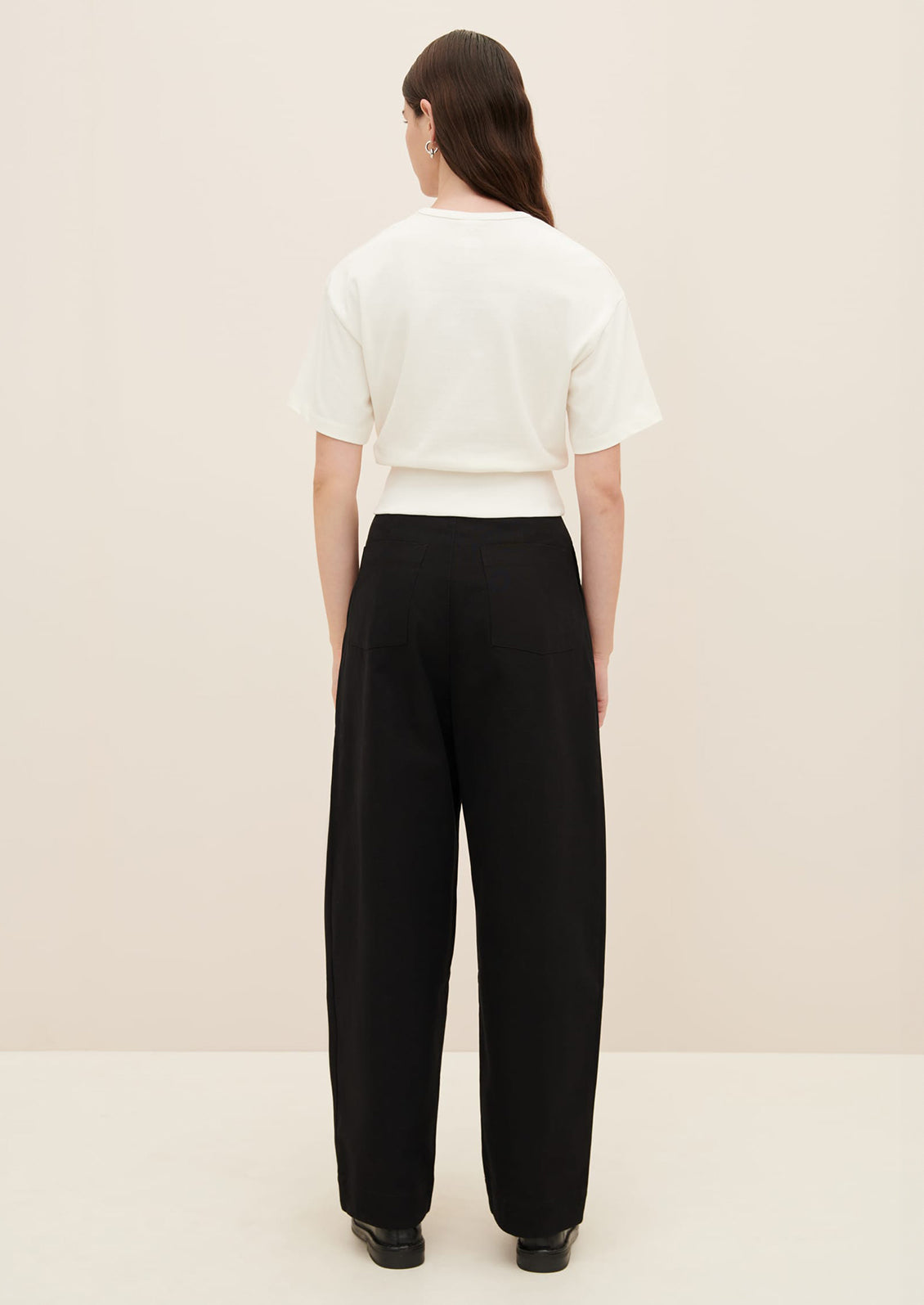 A woman wearing a boxy tee with short sleeves and fitted ribbed waistband, in white.