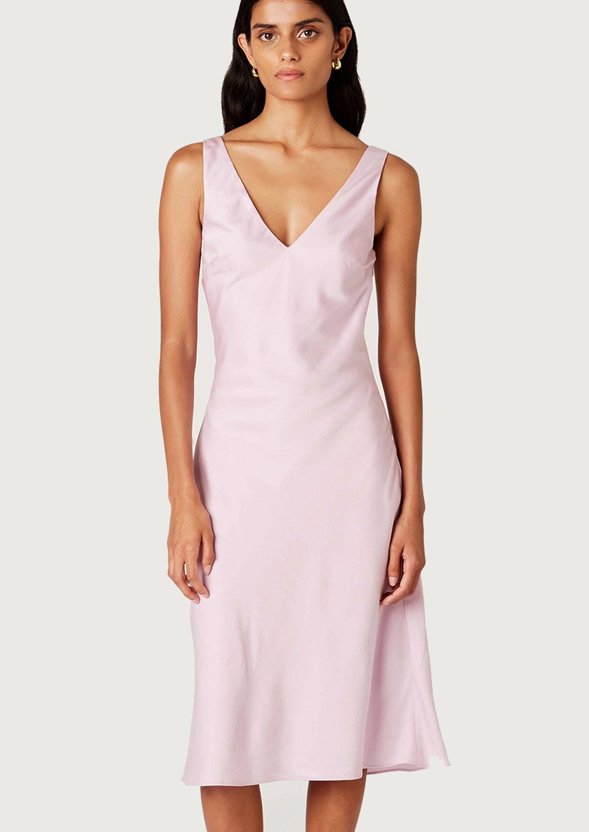 A woman wearing a satin v-neck sleeveless dress in ice pink.