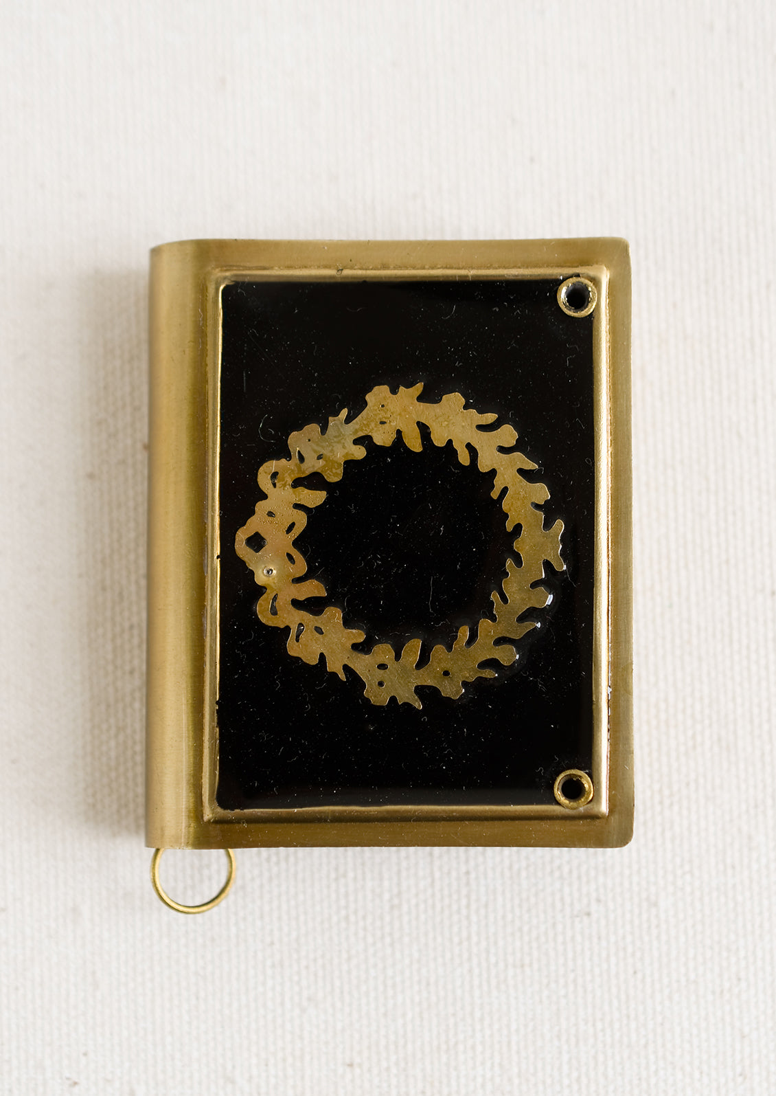 A book-shaped measuring tape with brass wreath design on black enamel.