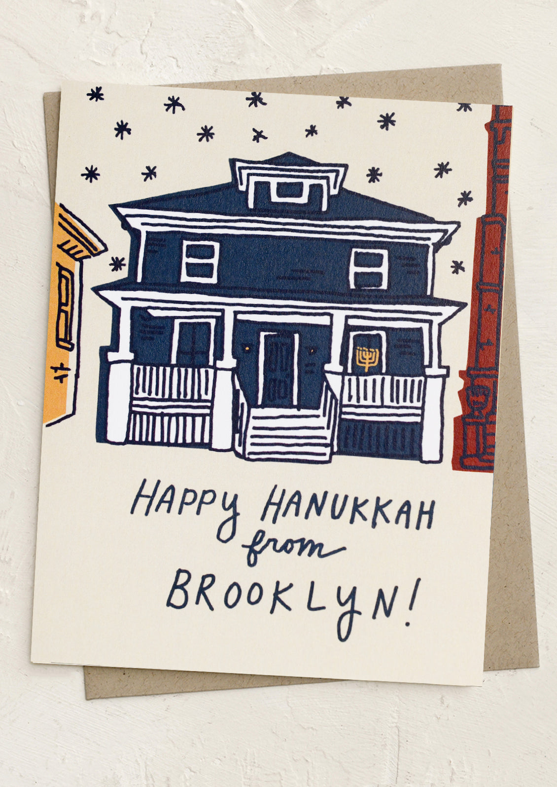 A greeting card with illustration of a house with a menorah in the window, text reads "Happy Hanukkah from Brooklyn!".