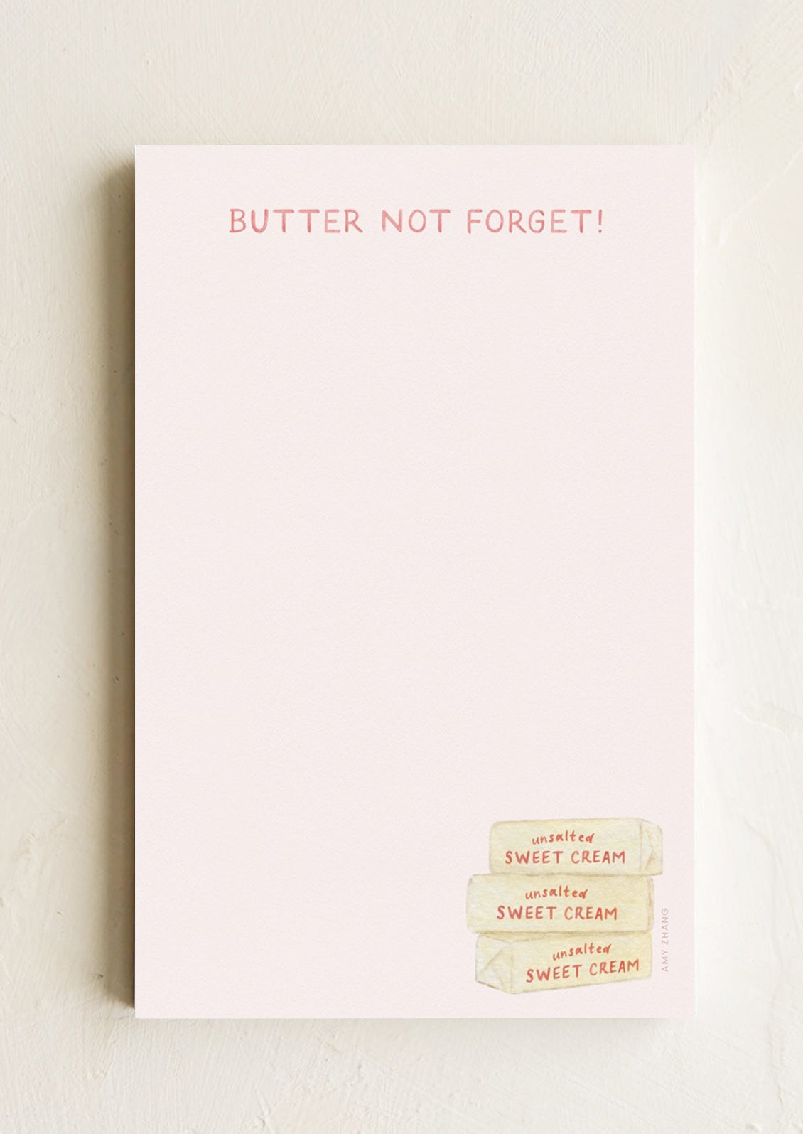 A pale pink notepad with butter illustration, text reads "Butter not forget!".