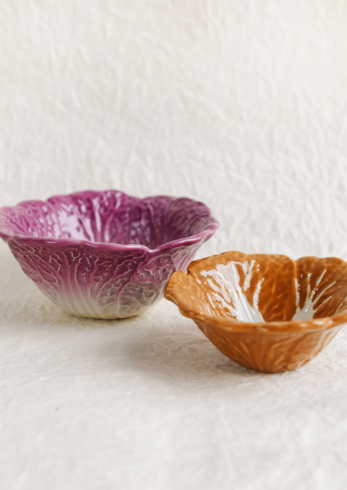 A pair of ceramic nesting bowls that look like orange and purple cabbage.