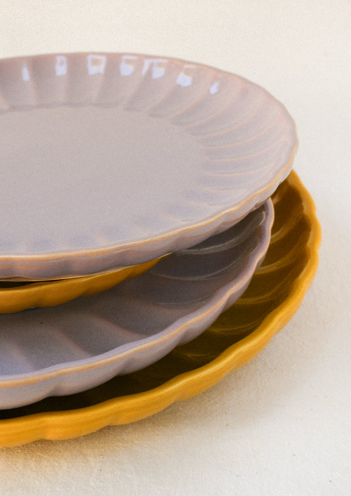 Mustard yellow and lavender ceramic plates stacked together, both with scalloped edges and glossy finishes.