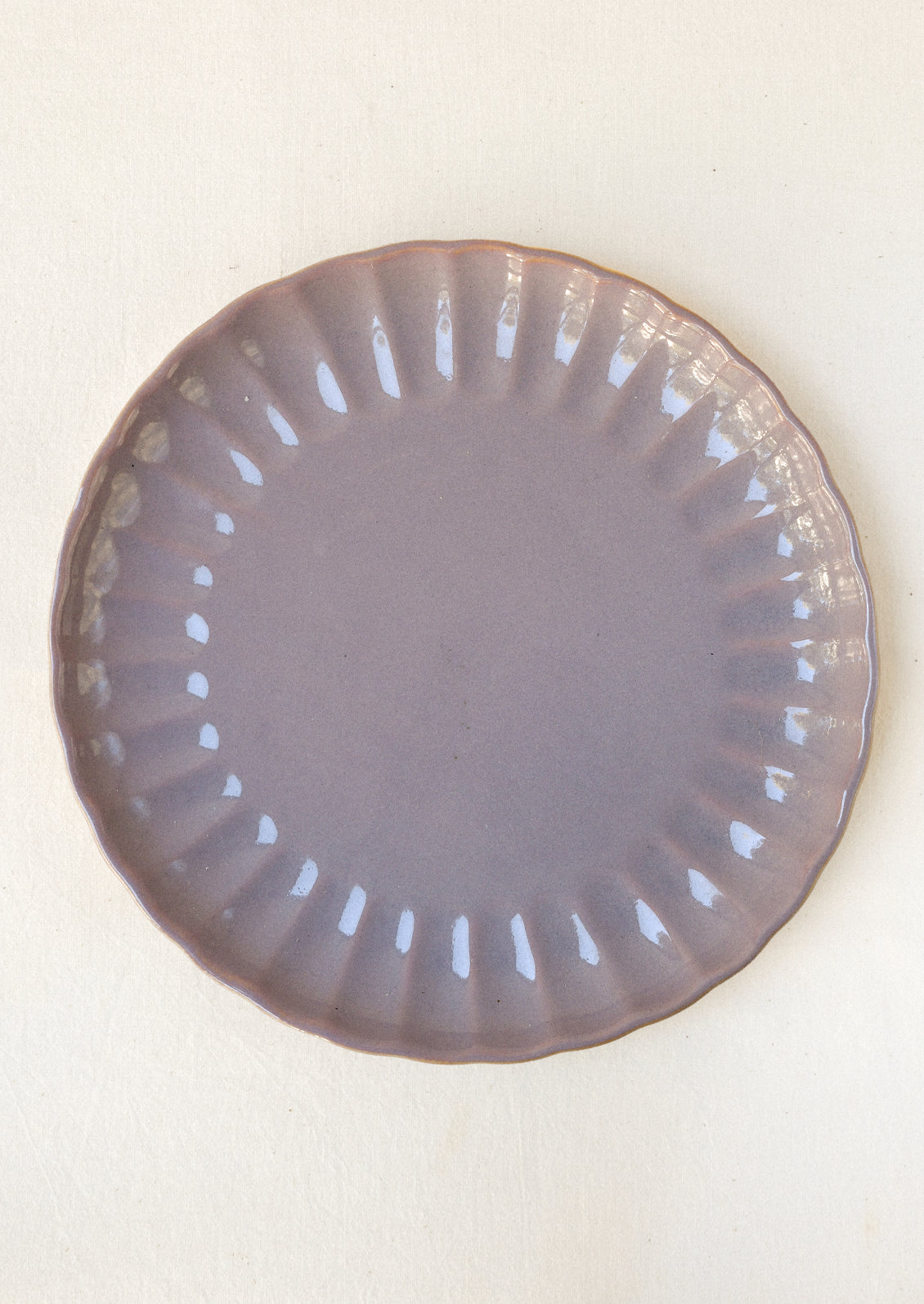 Lavender ceramic dinner plate with a scalloped edge and glossy finish, featuring a subtle ribbed pattern around the rim.