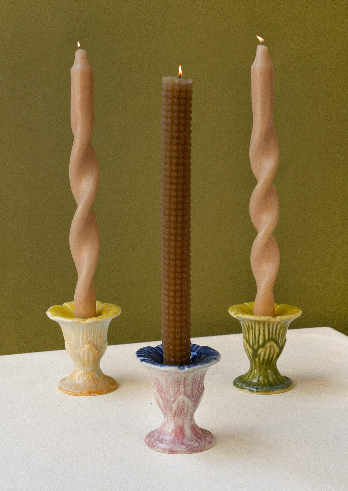 Three colorful flower-shaped ceramic taper candle holders each with a lit candle. 