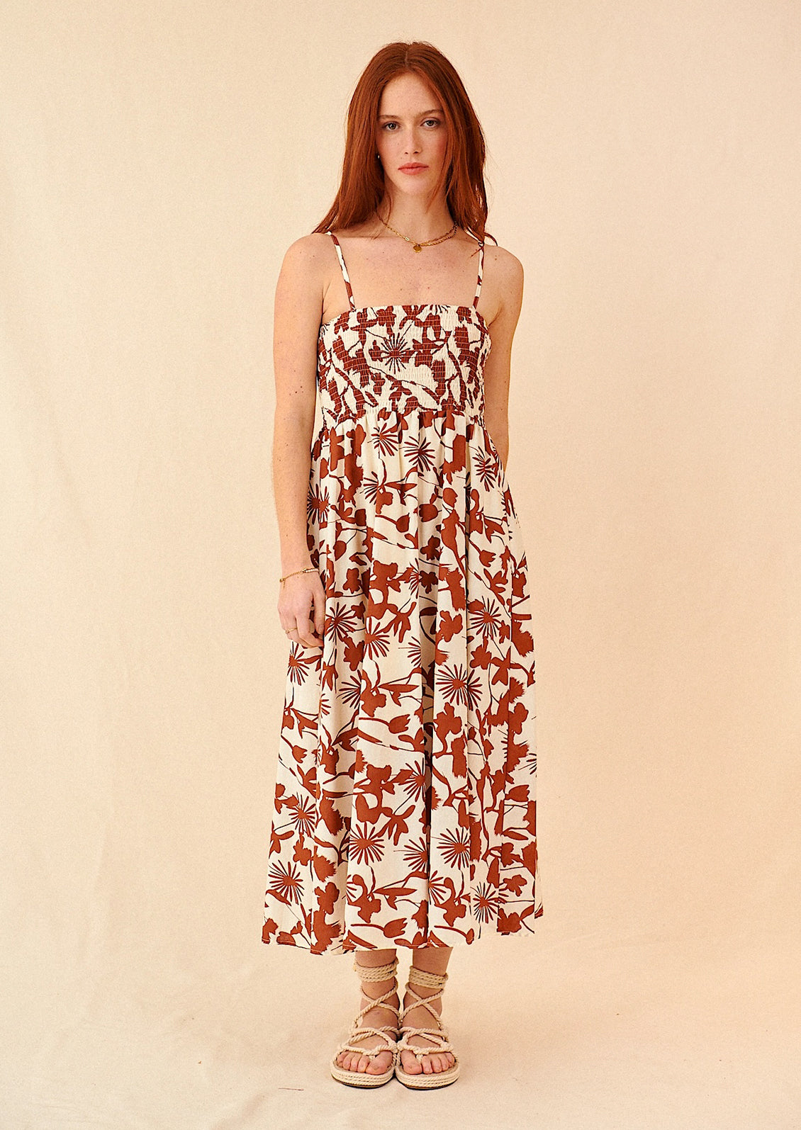 A woman wearing a sleeveless spaghetti strap dress in brown and white botanical print.