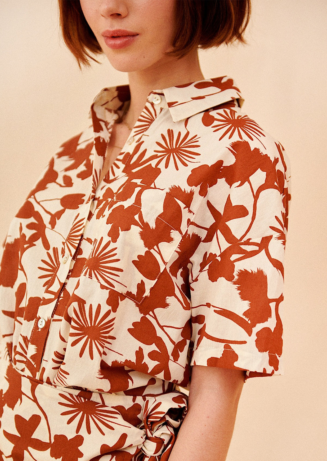 A woman wearing a short sleeve safari-style shirt in brown and white botanical print.