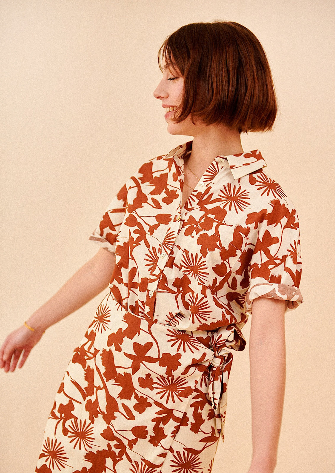 A woman wearing a short sleeve safari-style shirt in brown and white botanical print.