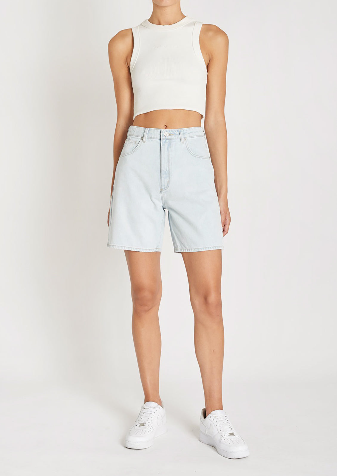 A woman in a white tank top, light-wash denim shorts, and sneakers. 