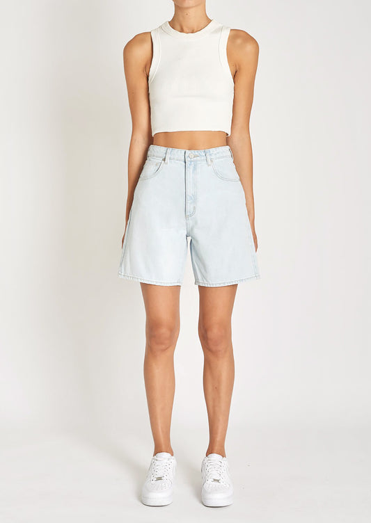 A woman in a white tank top, light-wash denim shorts, and sneakers. 