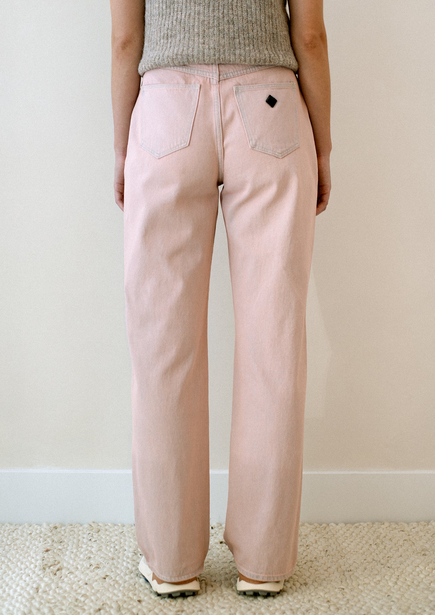 A woman wearing a pair of straight leg jeans in pink tinted wash.