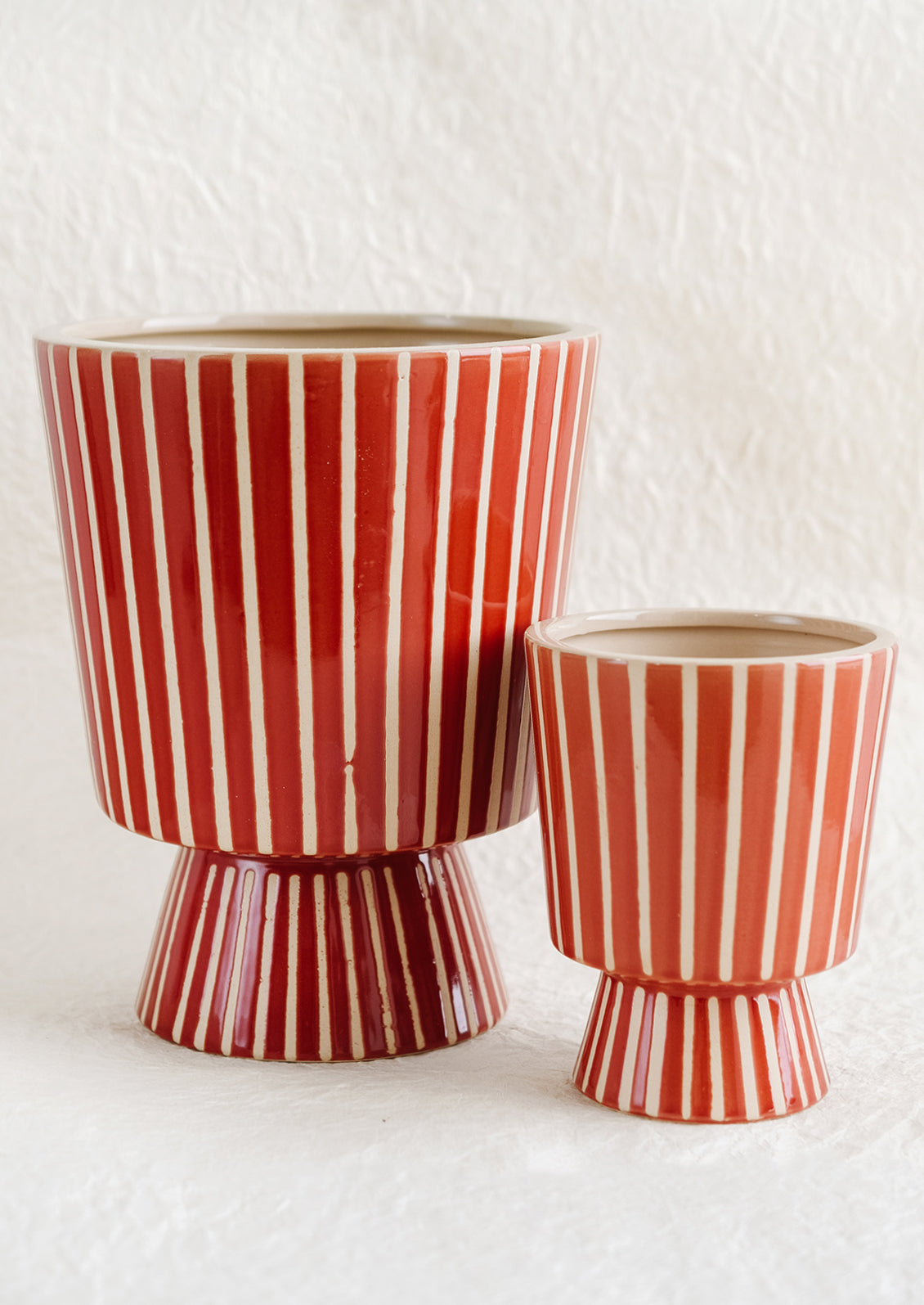 A footed planter with vertical white stripes on red ceramic, in small and large sizes.