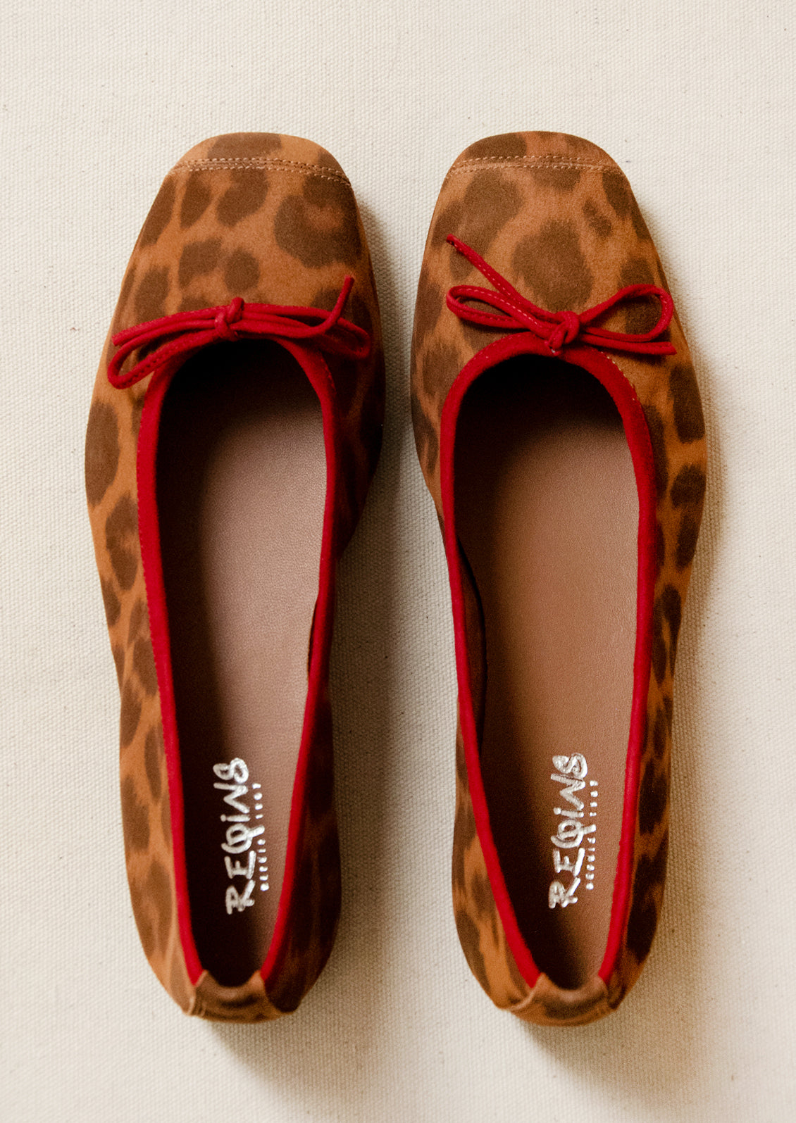 A pair of leopard print suede ballet flats with red accent.