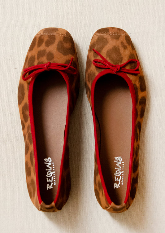 A pair of leopard print suede ballet flats with red accent.
