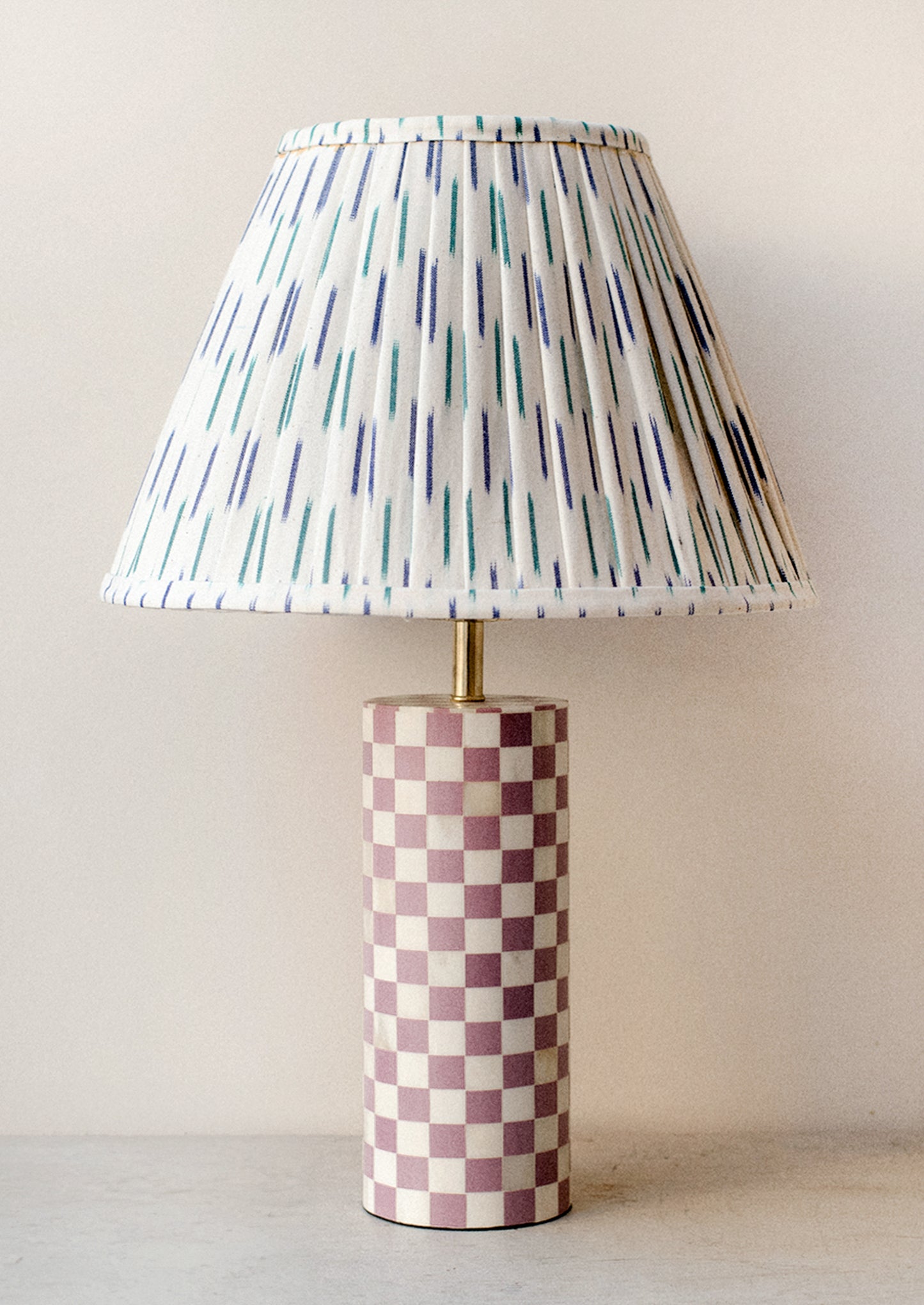 A table lamp with purple and cream checker print cylinder base with ikat printed pleated lampshade.