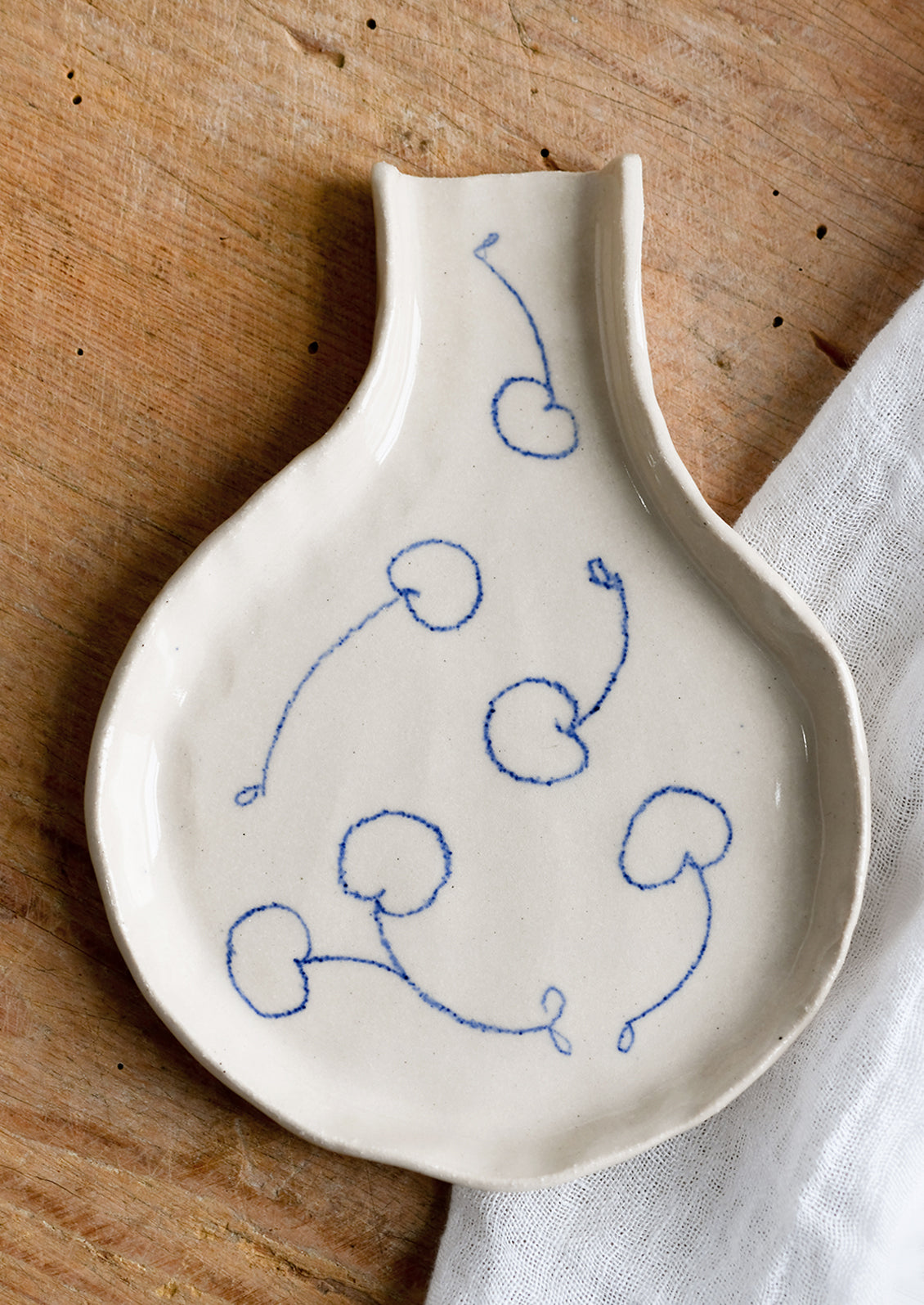 A handmade ceramic spoon rest with hand-drawn cherries in blue.