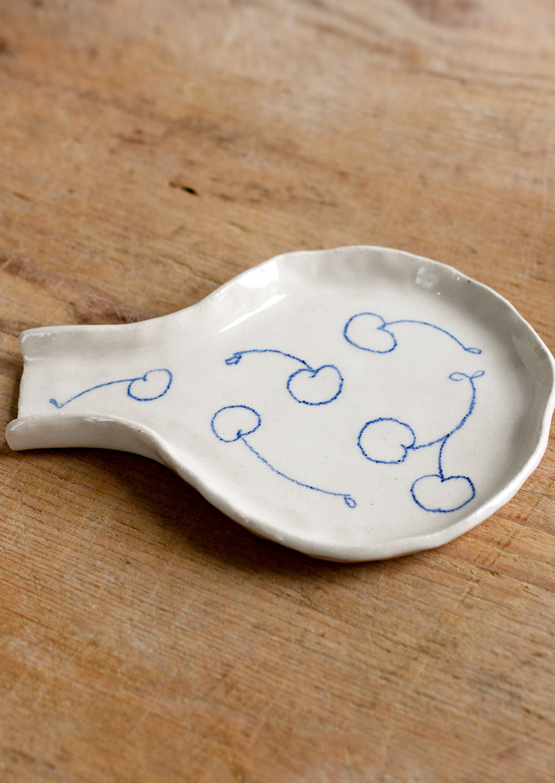 A handmade ceramic spoon rest with hand-drawn cherries in blue.