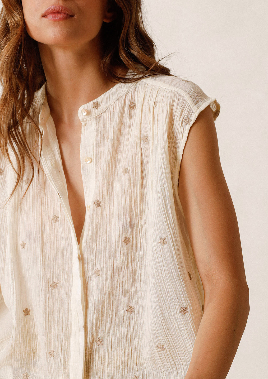 A woman in a white sleeveless top embroidered with grey stars. 