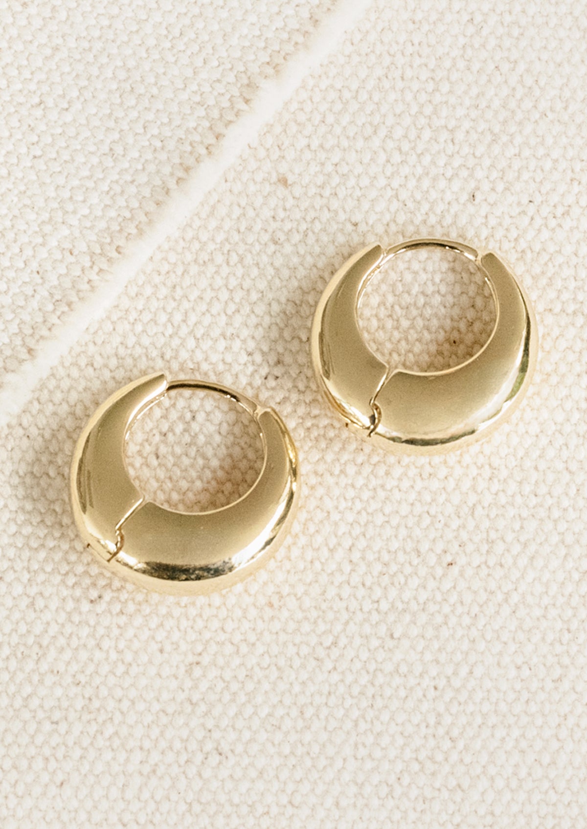Gold hoop earrings on a textured beige surface