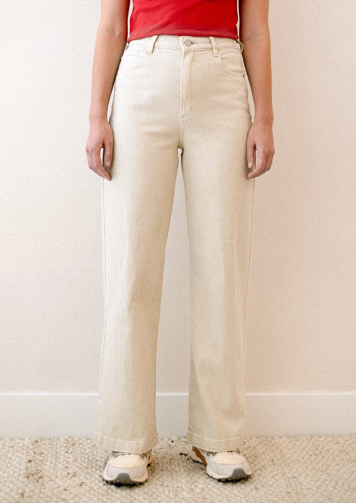 A woman wearing a pair of cream colored jeans with high rise and wide leg.