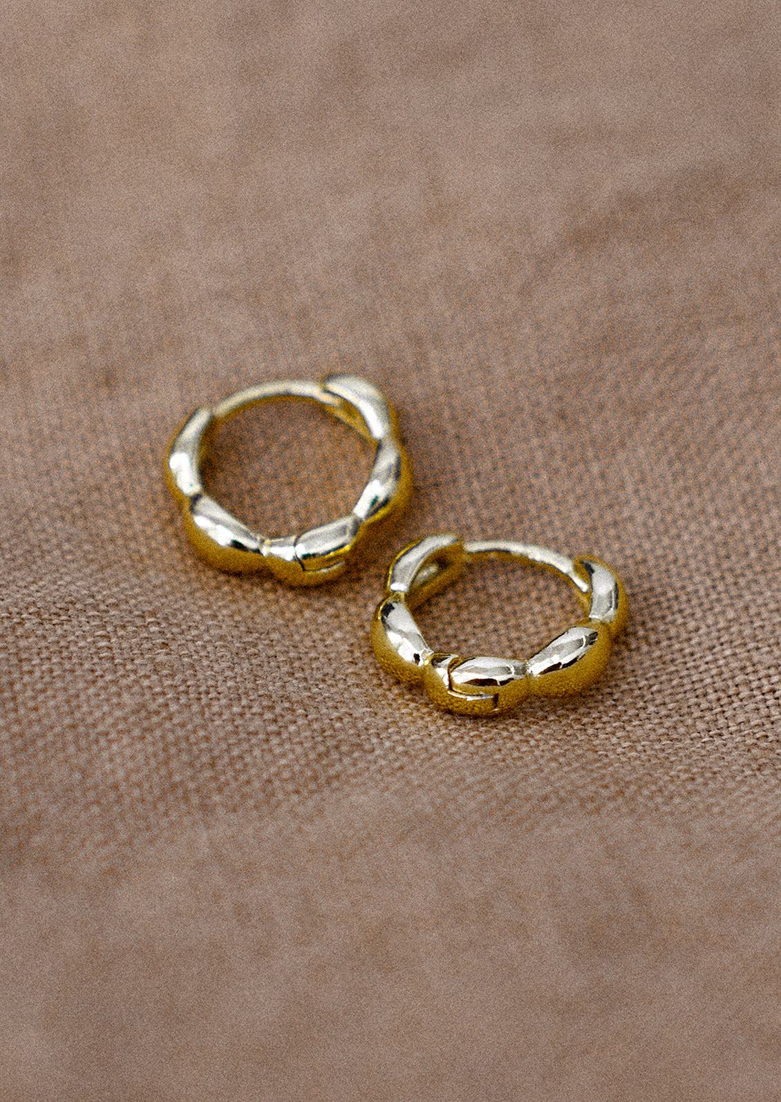 A pair of small gold huggie hoop earrings with scallop shape.