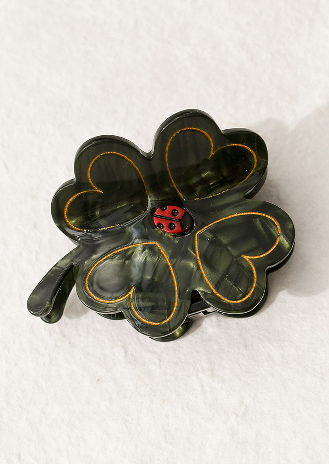 A hair claw in shape of green four leaf clover with small ladybug at center.