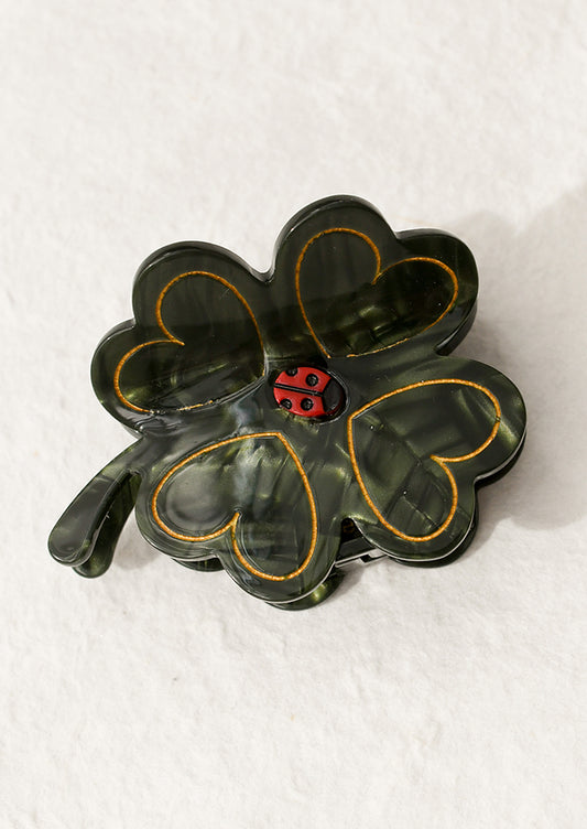 A hair claw in shape of green four leaf clover with small ladybug at center.