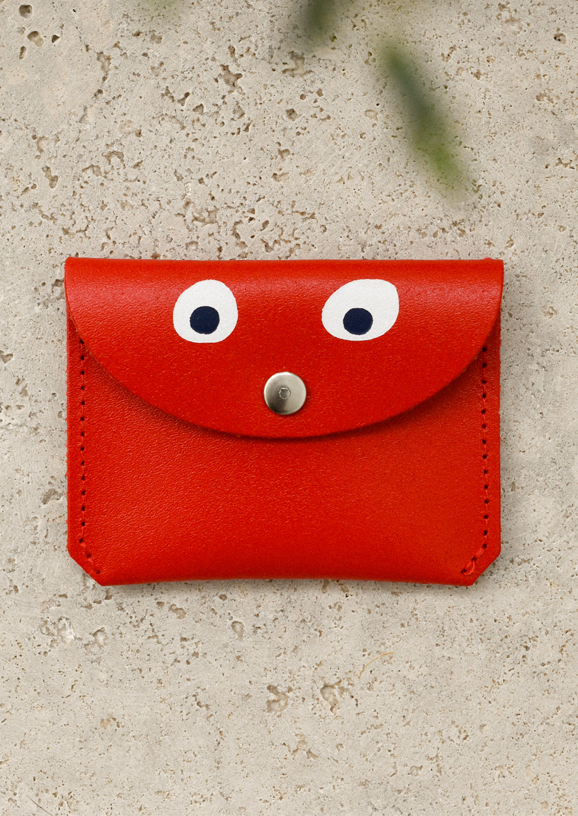 A red leather flap front coin pouch with hand painted googly eye detail.