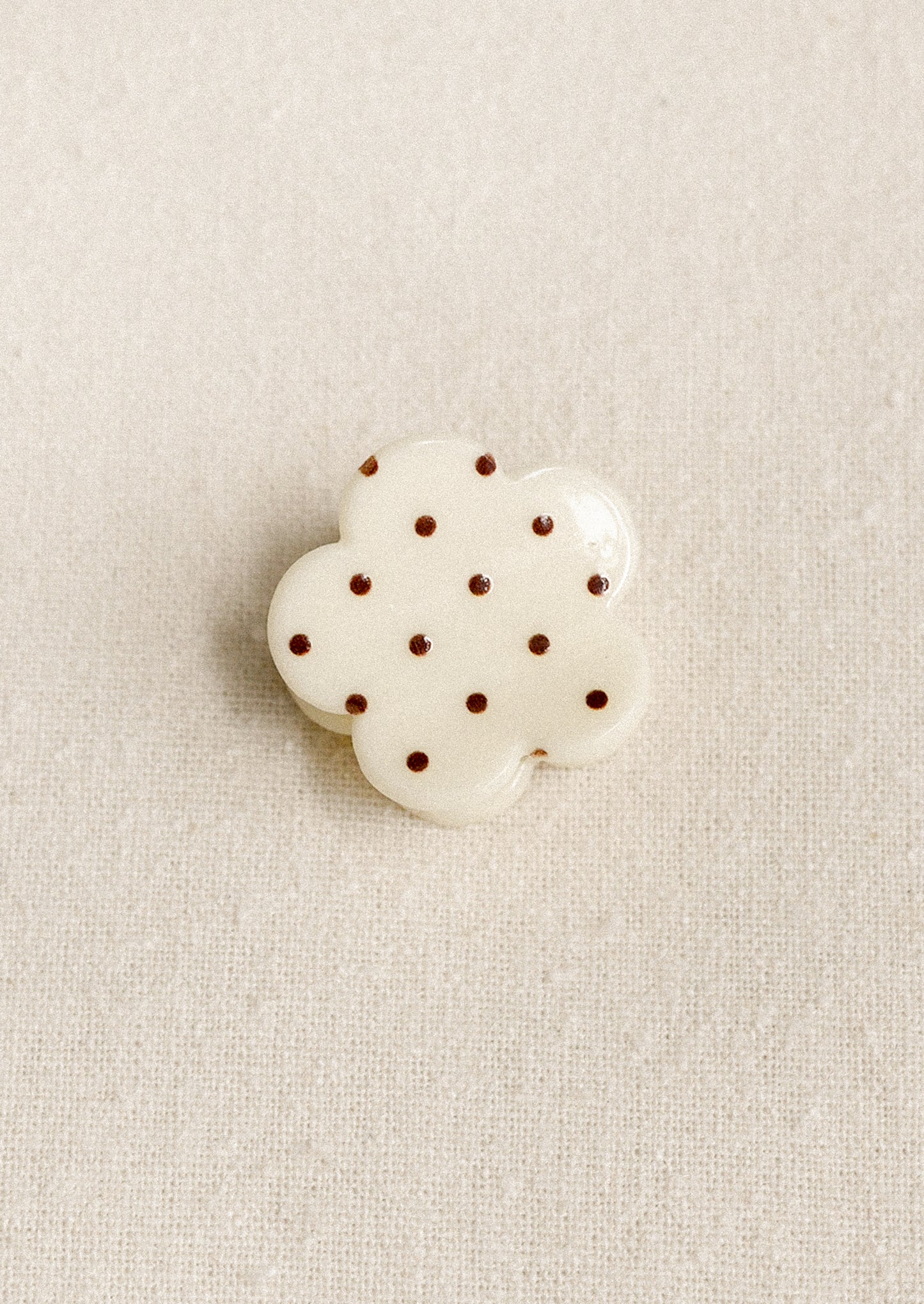 A small flower shaped hair clip in cream with burgundy polka dots.