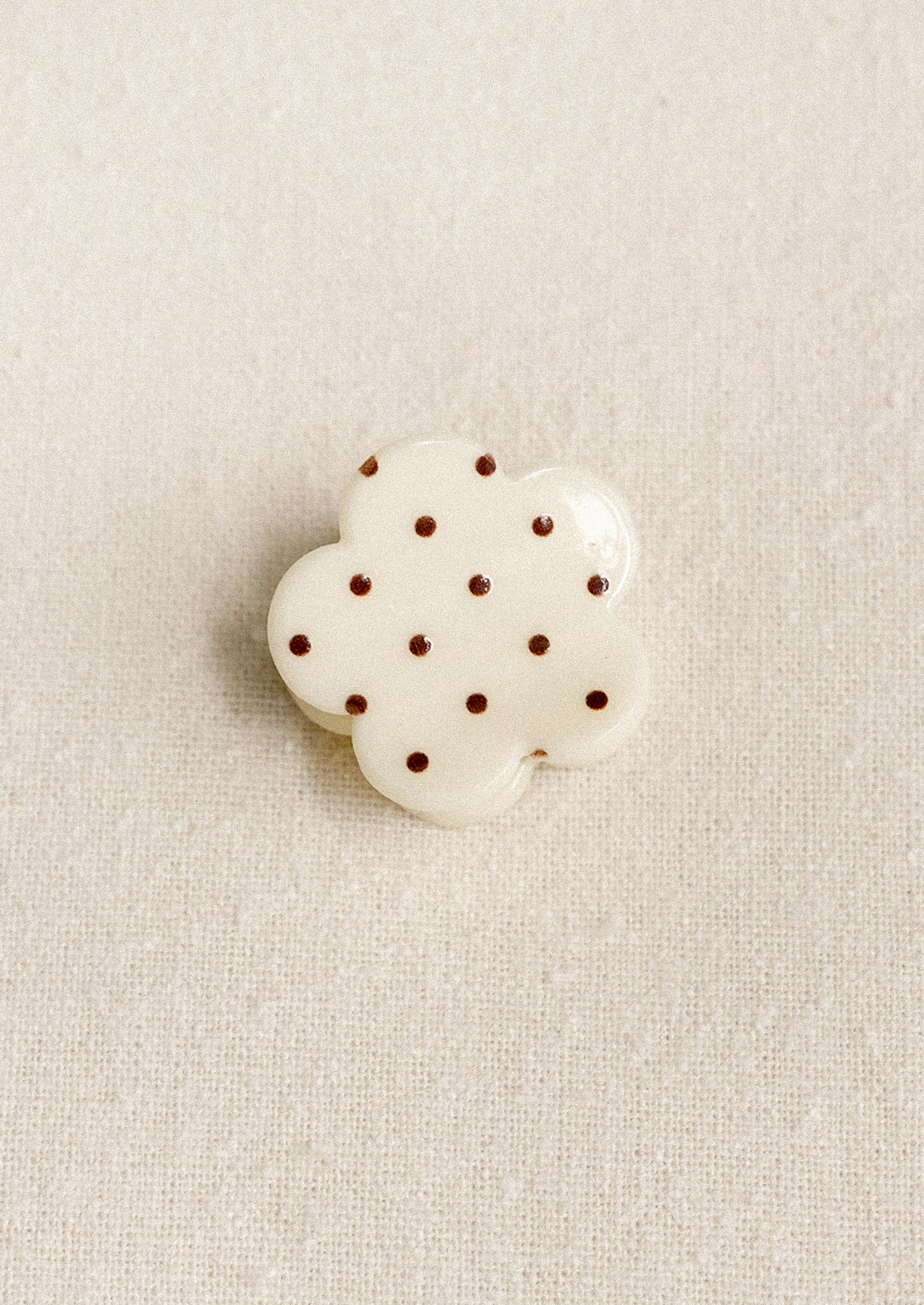 A small flower shaped hair clip in cream with burgundy polka dots.