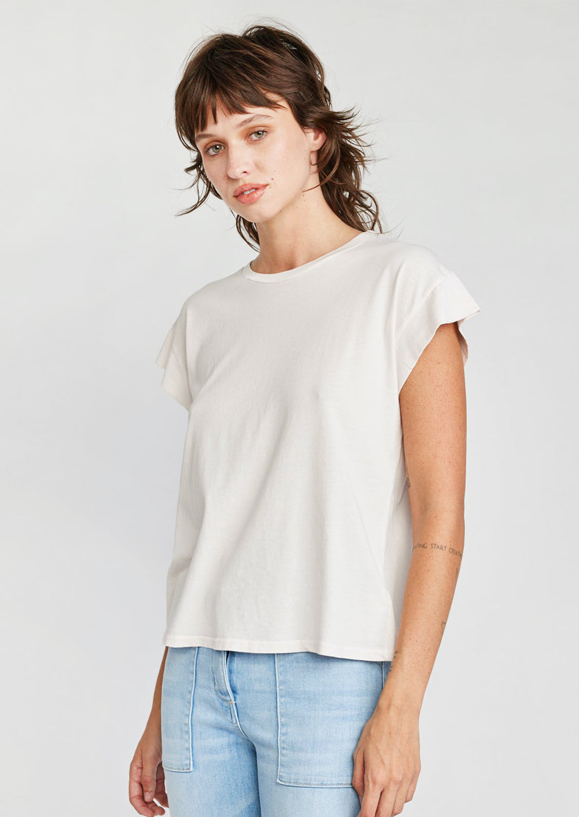 A woman wearing a cap sleeve muscle tee in cream color.