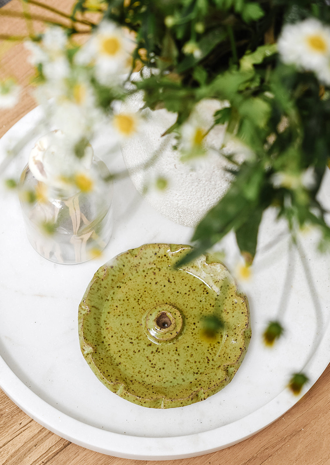 A green speckled incense holder on a tray with flowers and matches.