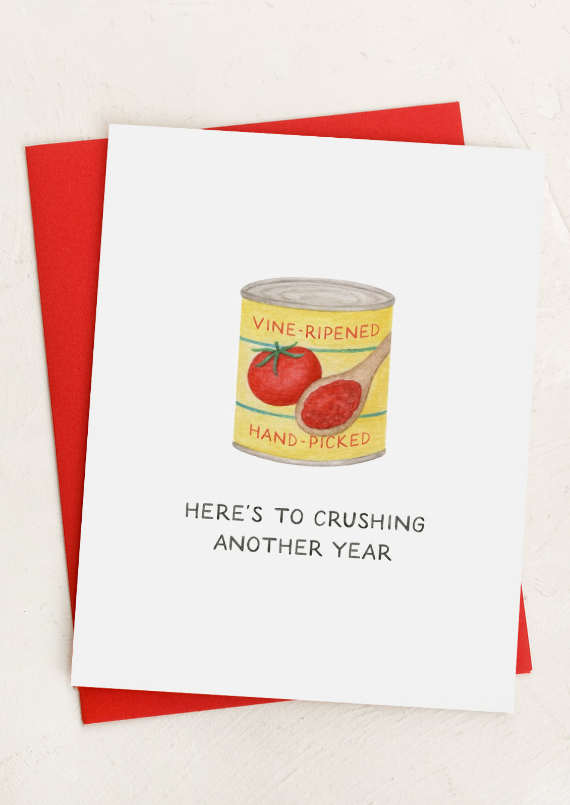 Greeting card with tomato can design and text 'Here's to crushing another year' on a red envelope.