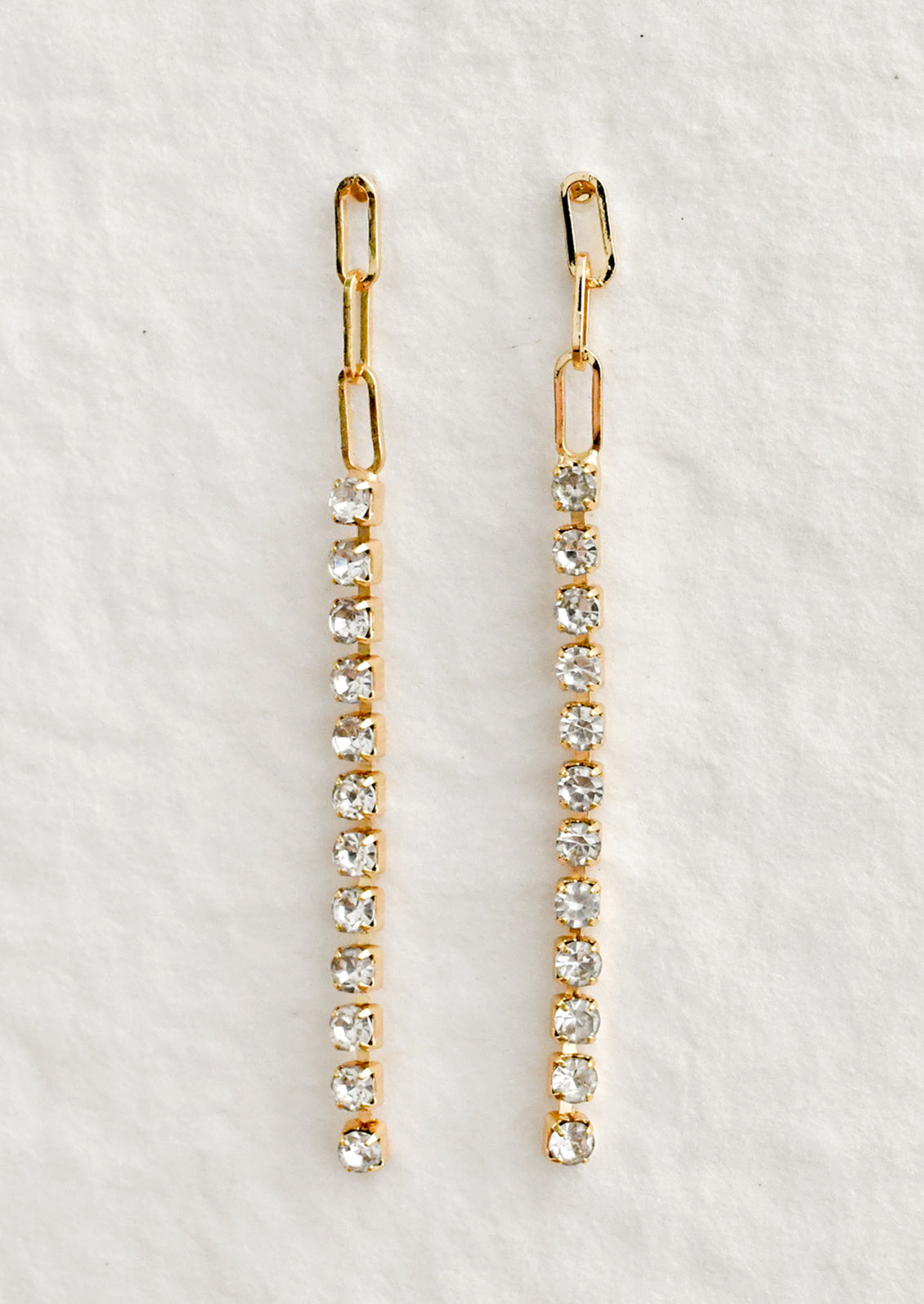 A pair of dainty earrings with paperclip chain top followed by tennis style crystals.